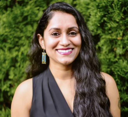 Megha Hegde headshot with a background luscious green bush