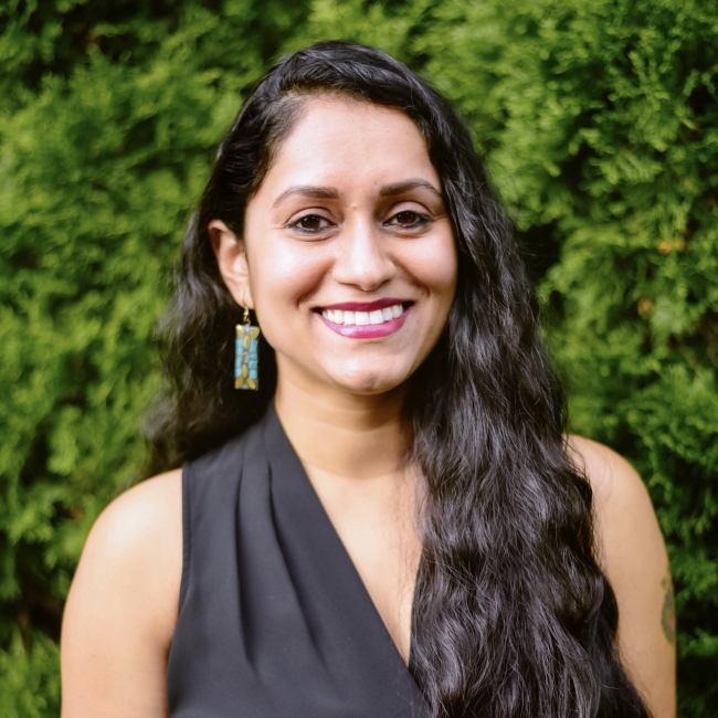 Megha Hegde headshot with a background luscious green bush