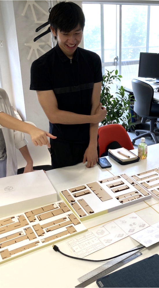 Michael Tan standing over a table with printed papers of brown blocks, discussing work with colleagues at KMDW