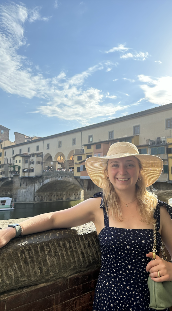 Kristen DiConza wearing a straw hat leaning against the stone bridge overlooking the Arno River in Florence, Italy 