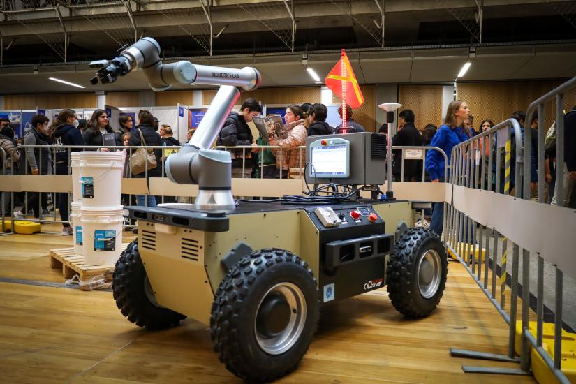 Mobile robotic arm displayed at the University of Melbourne's open day, protected by a barrier with students walking around on the outside of the barrier