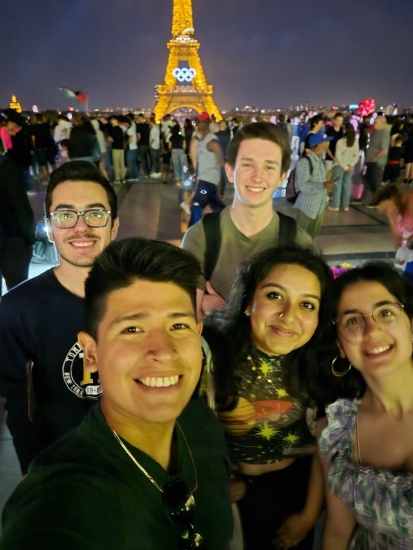 A selfie of Ian Rosado with other MIT students pictured with half of a lit up Eiffel Tower with the Olympic rings