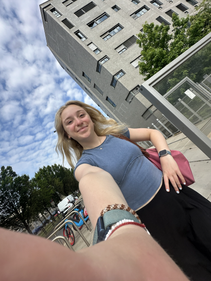 Kristen DiConza taking a selfie on a walk in Italy with a grey building and bike parking to the left